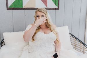 An emotional bride wipes away tears while seated in her wedding dress.