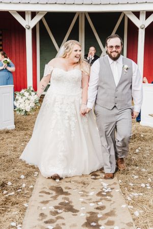 Newlyweds share a happy moment while walking down the aisle at their barn wedding.