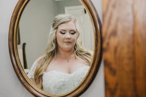 A bride looks at her reflection in an oval mirror while getting ready.