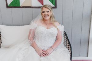 A beautiful bride poses in her lace wedding gown while seated on a white couch.