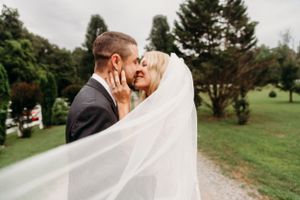 A romantic wedding moment captured through flowing veil in a garden setting.