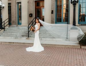 Bride in elegant white gown poses on stone steps of classic brick building.