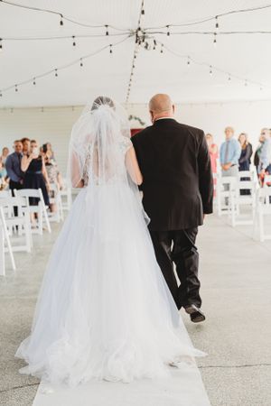 A wedding ceremony scene showing the walk down the aisle under string lights in an elegant white tent setup.