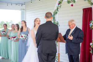 A wedding ceremony takes place at a covered outdoor venue with mint green bridesmaids and floral pergola decorations.