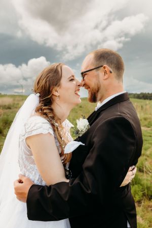 A bride and groom share a joyful moment together outdoors in a field under dramatic clouds.