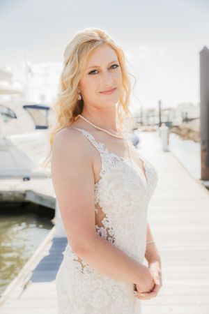 A bridal portrait on a sunny marina dock featuring a white lace wedding gown and pearl necklace.
