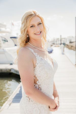 Beautiful wedding portrait taken at a marina dock featuring a white lace dress and pearl necklace with boats in background.