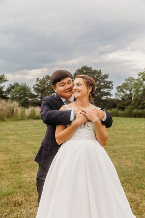 Couple embraces in joyful moment on grassy field during wedding photoshoot.