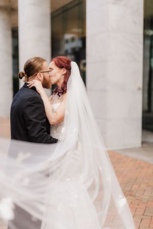 Wedding couple shares tender moment with flowing veil by classical architecture.
