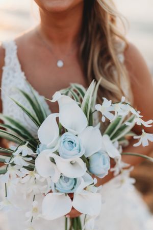 Bridal bouquet featuring white calla lilies and light blue roses with tropical greenery.