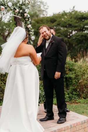 An emotional first look moment between newlyweds under a floral arch.