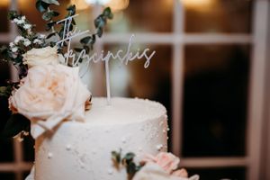 Close-up of a white wedding cake decorated with pale pink roses and a script topper.