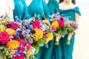 Vibrant rainbow bouquets with pink roses and blue flowers contrast against teal bridesmaid dresses.