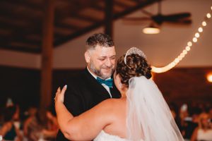 Dancing couple embraces during wedding reception under string lights.