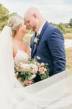 Romantic wedding portrait through flowing veil with soft pink bouquet.