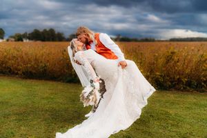 Dramatic wedding photo showing couple in white dress and suit dipping pose in golden field at sunset.