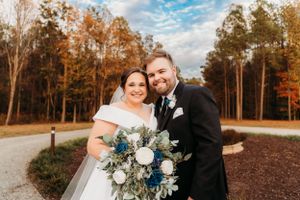 A happy couple sharing a moment with their blue and white bouquet against fall trees.