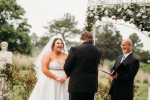 A wedding ceremony under a floral arch with the couple and officiant sharing a joyful moment.