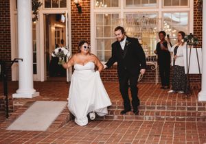 A joyful wedding couple exits their venue on brick steps decorated with white columns.