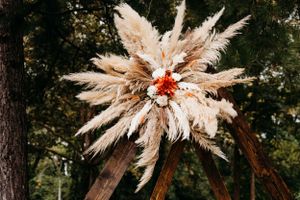 Large bohemian floral arrangement with pampas grass and orange flowers against forest backdrop.
