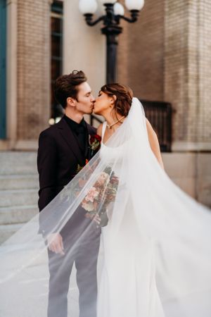 Romantic wedding kiss with flowing veil against classic architecture.
