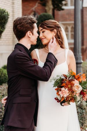 Tender wedding moment captured outside brick church with autumn-themed floral bouquet.