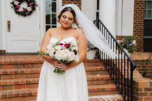 A bride in a strapless white gown holds a stunning bouquet of white and burgundy flowers.