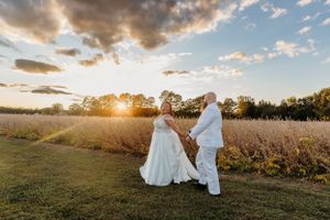 Bride and groom walking hand in hand through a field during golden hour sunset.