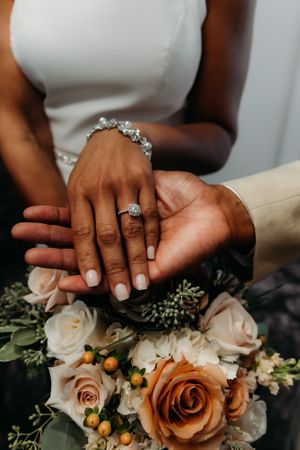 Wedding rings and jewelry showcase on hands with a romantic peach and cream rose bouquet.