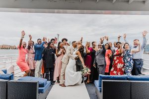 Large wedding party celebrates on boat deck with skyline backdrop.