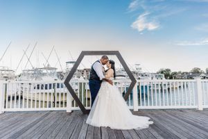 Wedding couple posing under geometric arch with marina and boats in background.