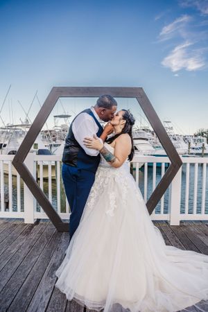 Newlyweds sharing a romantic kiss under a hexagonal arch on a marina deck.
