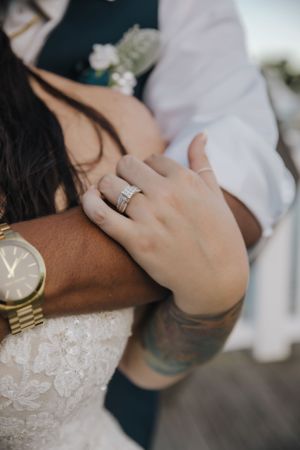 Close up of wedding rings and gold watch as couple embraces.