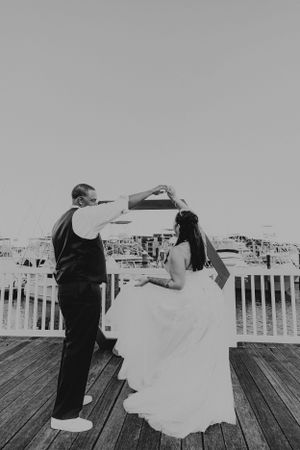 Wedding couple dances on wooden dock in black and white photo.