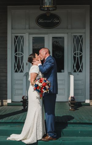 Romantic wedding kiss at entrance of Rosemont Inn with patriotic bouquet.
