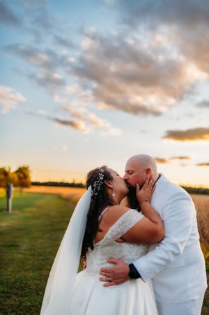 A romantic sunset wedding kiss with dramatic clouds and a flowing white veil.