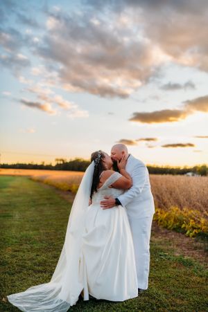 Newlyweds share an intimate moment at sunset in a field with dramatic sky.