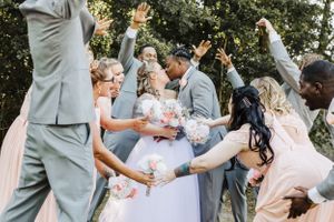 Wedding party celebrates with joy and raised hands during outdoor group photo.