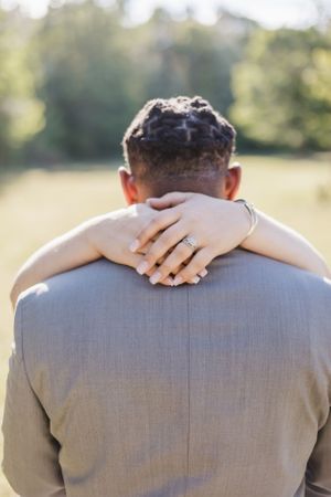 Close-up of wedding ring and hands embracing on groom's grey suit jacket.