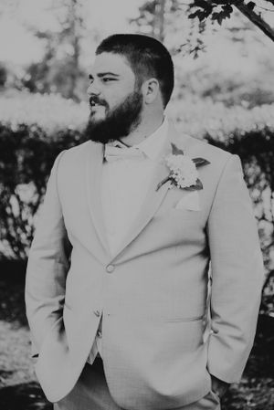 Black and white portrait of groom in light colored suit with boutonniere.