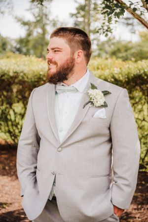 Groom wearing light gray suit with white bowtie and boutonniere.