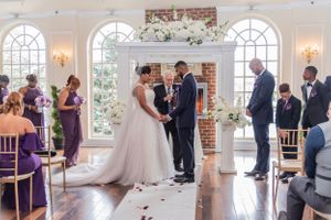 Indoor wedding ceremony in elegant venue with arched windows and purple decor.