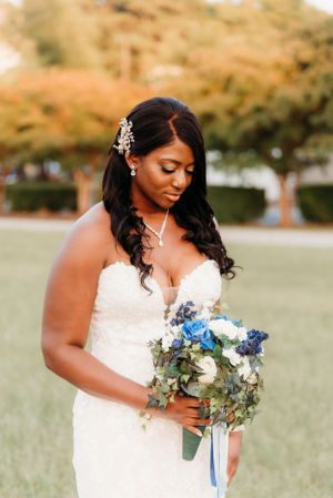 Elegant bride in white lace gown holds blue and white bouquet during golden hour photography session.