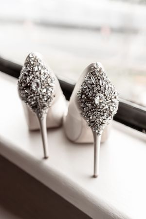 Elegant bridal shoes with crystal-embellished heels displayed on a windowsill.
