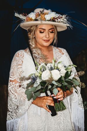 A stunning lace wedding gown paired with a decorated wide-brim hat and white floral bouquet.