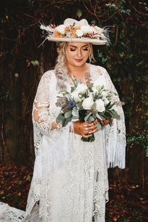 A close-up shot of a wedding dress with delicate lace details and a bouquet featuring white flowers and greenery.