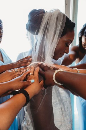 Helping hands assist with buttoning up a wedding dress while a delicate veil flows in the background.
