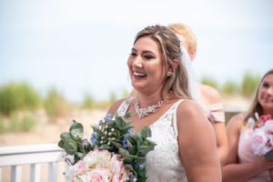 Joyful bride wearing lace dress holds pink and green bouquet while laughing on her wedding day.