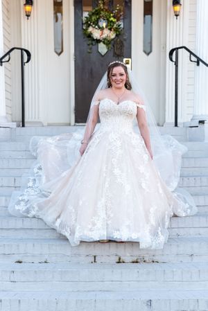 Bride in lace off-shoulder ballgown poses on white mansion steps.