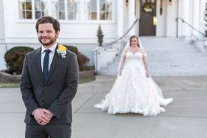 First look wedding photo in front of white mansion with groom in foreground and bride in distance.